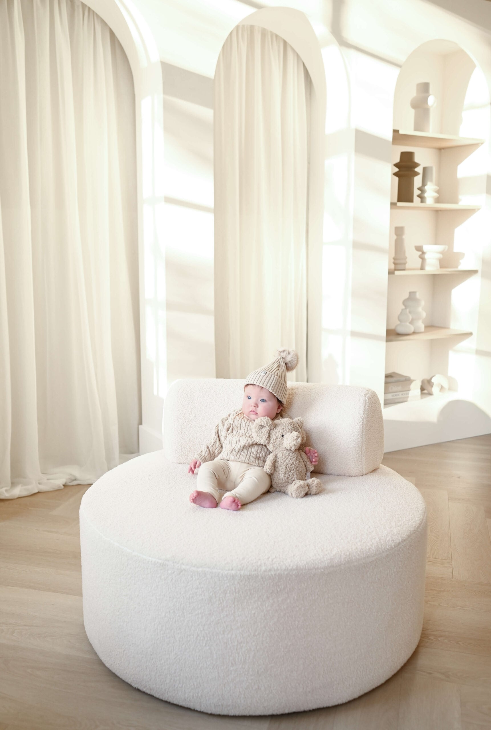 Baby in gebreid pakje op ronde poef in studio – Studio Roos Fotografie