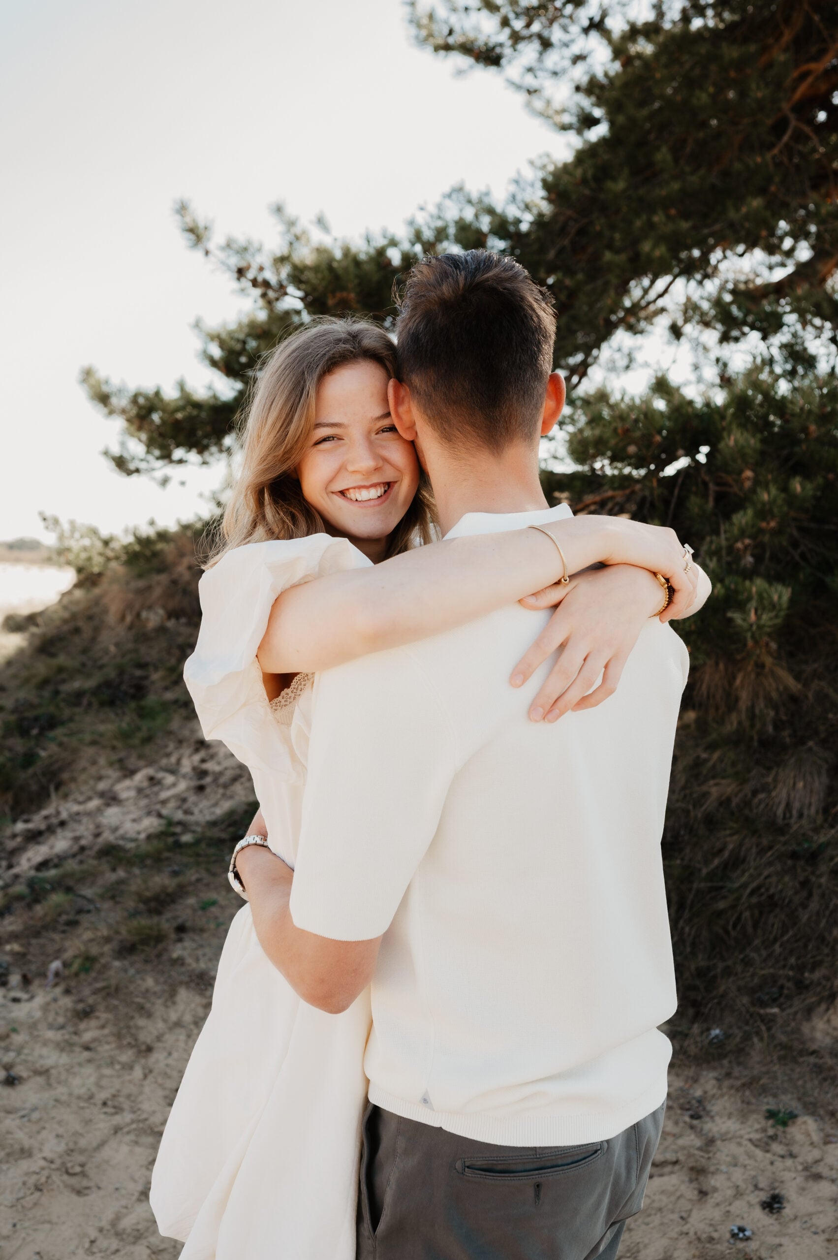 Lachende vrouw omhelst haar partner in de duinen – Studio Roos Fotografie