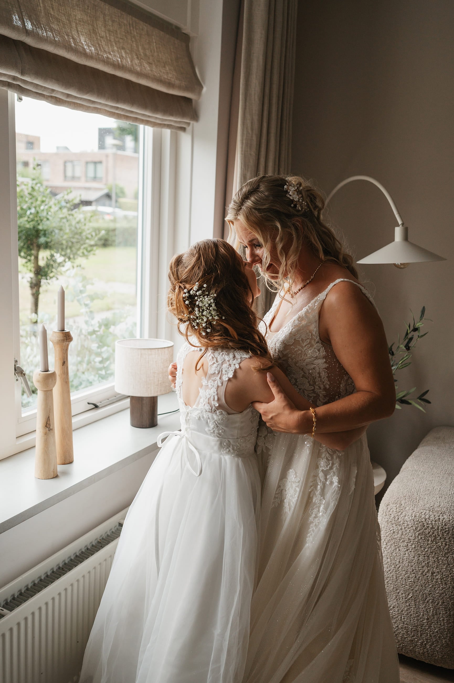 Bruid en bruidsmeisje samen bij het raam tijdens het aankleden – Studio Roos Fotografie