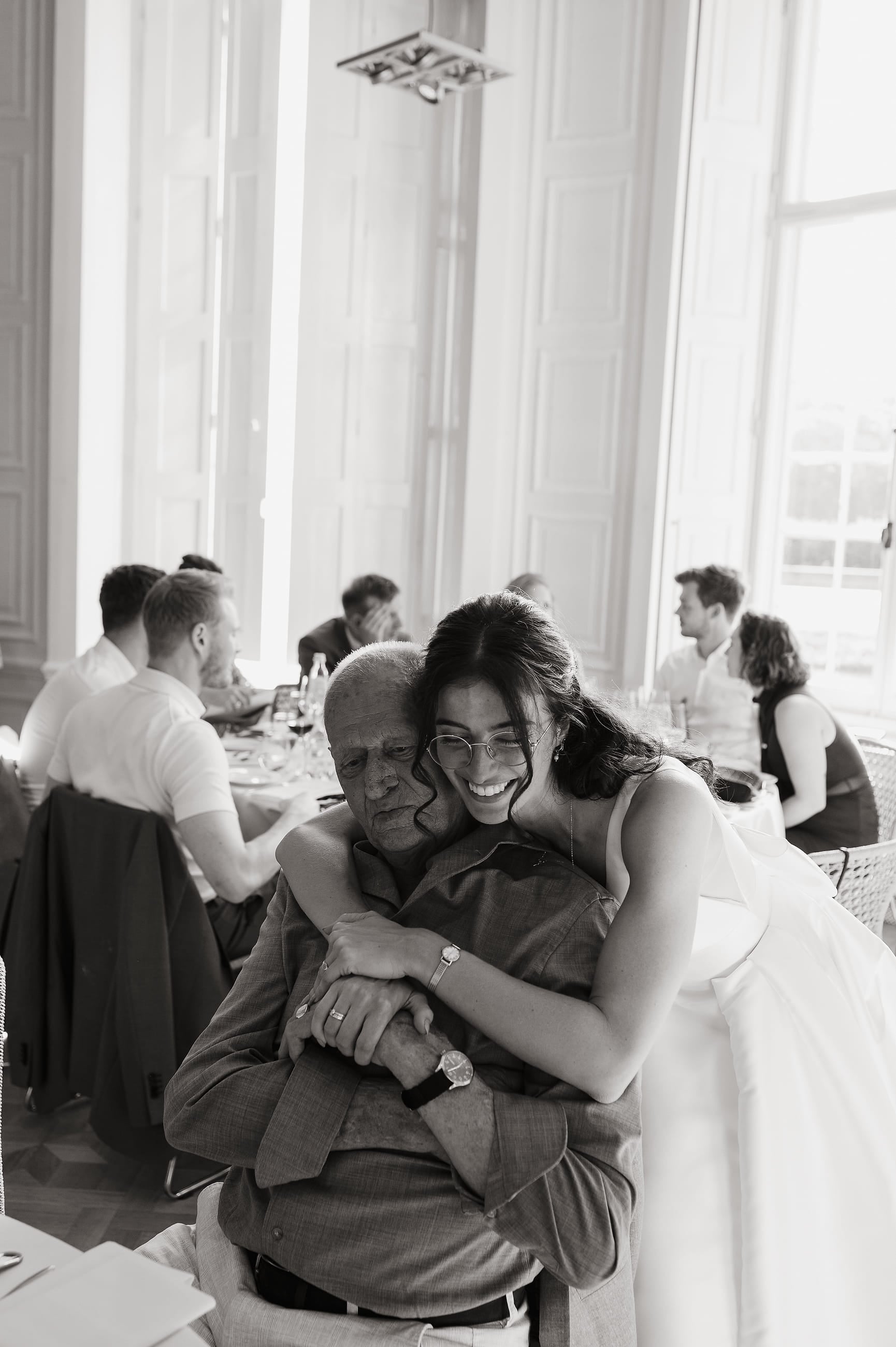 Bruid omhelst een gast tijdens het diner, zwart-wit – Studio Roos Fotografie