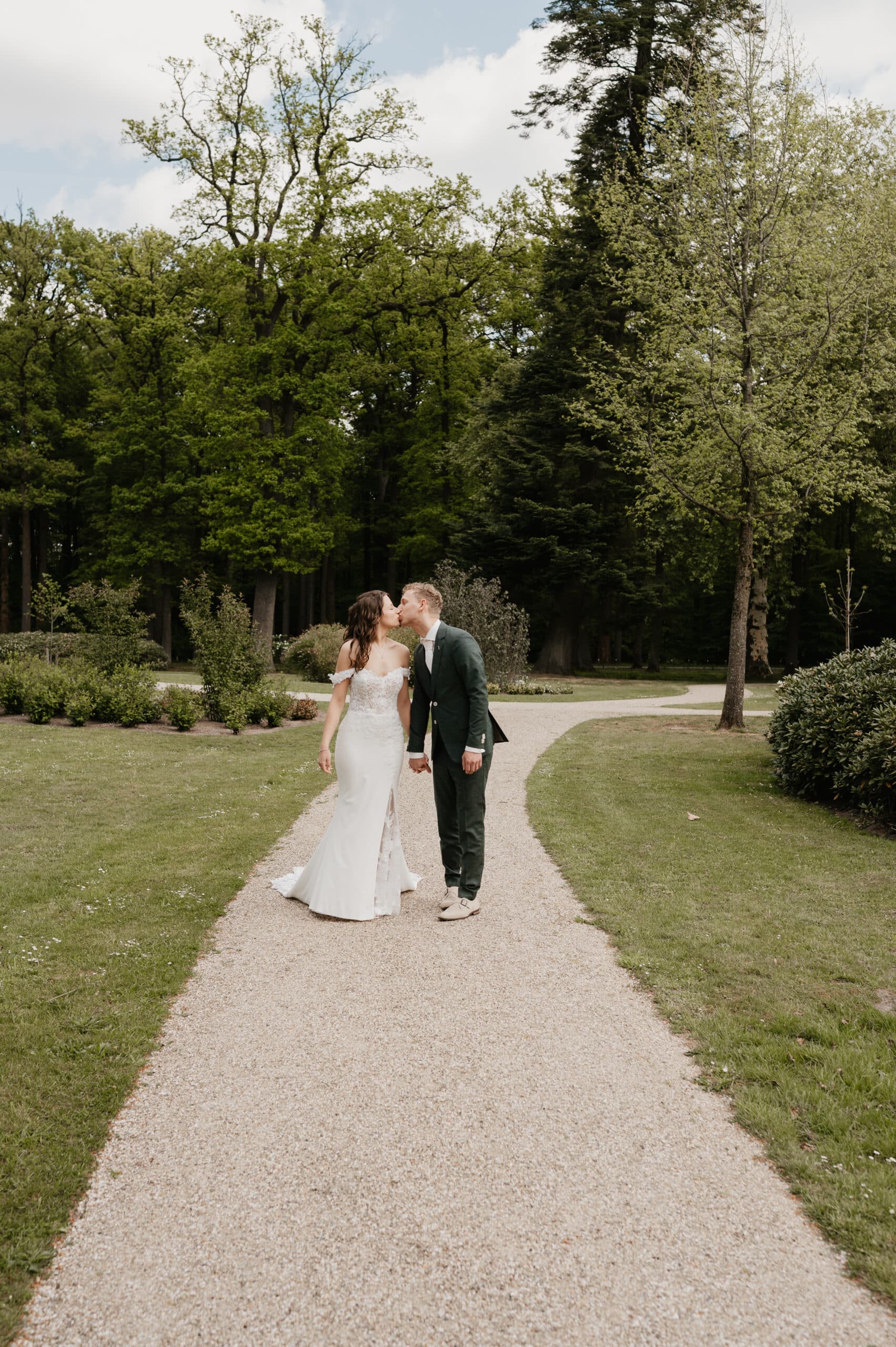Bruidspaar kust elkaar op een parkpad – Studio Roos Fotografie